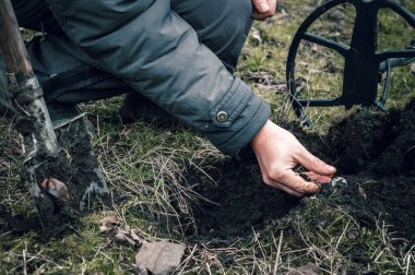 The coin is a lucky find while searching for treasures with a metal detector in the field. The man's hand takes the found ancient coin.