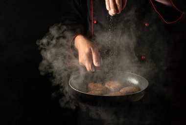 Bir şefin elinde sıcak tavada et bifteğine tuz eklemek. Hamburger için köfte pişiriyorum. Menü veya tarif için boşluk.
