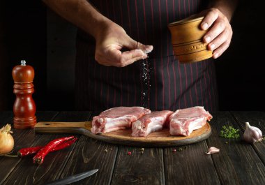Professional chef salts raw sliced meat steaks on the cutting board of the kitchen before preparing dinner. Delicious grill idea. Copy space