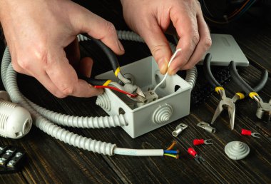 The electrical connection in the workshop of a master electrician. Close-up of the hands of an electrician during work. Cutting a cable or wire in a gray junction box
