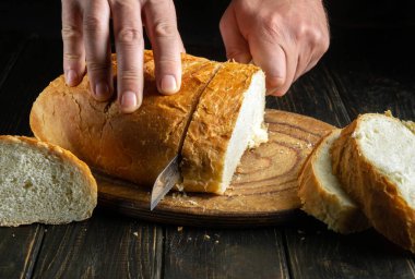 The hands of the chef cut fresh wheat bread with a knife to prepare sandwiches for a snack. The concept of traditional food or national dish. Copy space