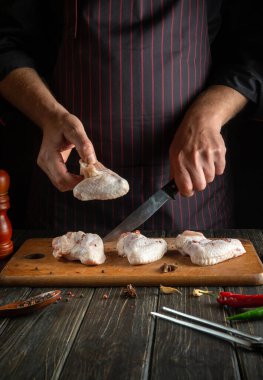 Professional chef prepares chicken nugget with raw chicken wings in the kitchen. Space for advertising on a dark background