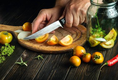 Chef hands with a knife cut tomatoes on a cutting board. Preparation of canned vegetable salad. Copy space