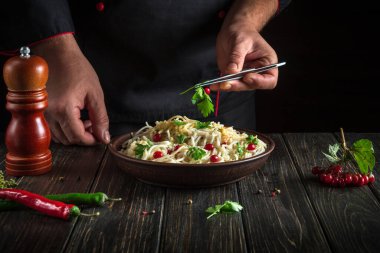 The chef adds greens to a bowl of spaghetti in the kitchen. Delicious pasta with vegetables and spices