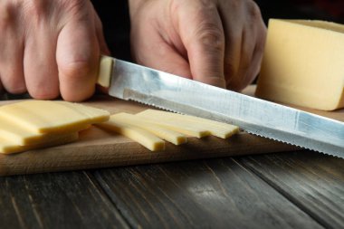 Close-up of a chef hands with a knife slicing cheese on a cutting board in a restaurant kitchen. Preparing dairy food for breakfast while on a diet.