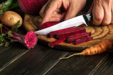 Slicing beets or beetroot by the hands of a cook on a cutting board for cooking diet food in the kitchen. Peasant products. Copy space