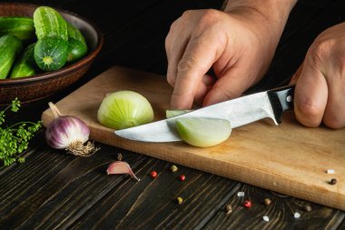 Slicing onions on a cutting board with the hands of a chef for preparing a vegetable salad. Menu for a restaurant or hotel on a dark background