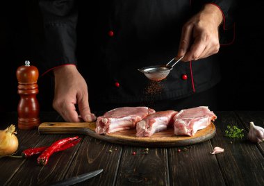 Professional chef sprinkles fresh ribs with paprika close-up. Dark background for a recipe book or menu in a hotel