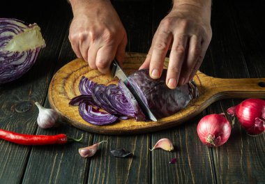 The cook cuts red cabbage on a cutting board with a knife. Cooking vegetable salad in the kitchen. The idea of a vegetable diet from peasant products.