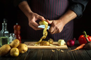 Professional chef with a knife cleans potatoes in the kitchen. Hands of a cook with a knife while preparing delicious food. Vegetable diet menu for restaurant or hotel