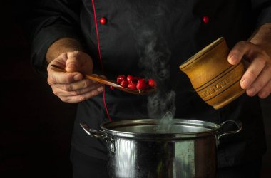 A person adds dry rose hips to boiling water in a pot to make a medicinal tea. Folk medicine idea with space on black background