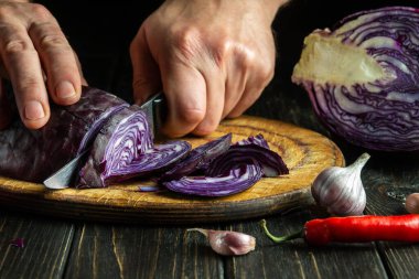 Hands of a chef with a knife cut red cabbage on a cutting kitchen board. Cooking vegetable salad in the restaurant kitchen. Vegetable diet idea