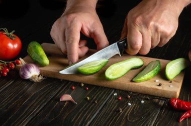 Hands of a cook with a knife  cut fresh cucumbers for pickling with spices and vegetables. Close-up of a chef hands while working on a kitchen table in a restaurant. Copy space