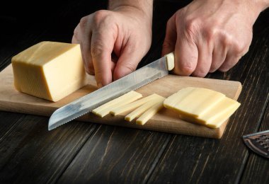 Aşçı elinde bıçakla sandviç, italyan pizzası ya da mutfakta atıştırmak için tahta tahtada peynir kesiyor. Yemek hazırlığı. Sağlıklı beslenme ve yaşam tarzı. Yiyecek konsepti