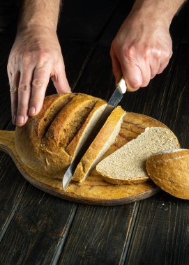Bıçaklı bir aşçının elleri tahtanın üzerinde buğday ekmeği kesiyor. Mutfak masasında buğday ekmeği mi yoksa sağlıklı beslenme ve geleneksel fırın konsepti mi?