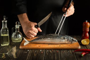 Aşçı mutfakta Scomber veya uskumru pişirir. Restoran ya da otel için balık yemi pişirme fikri. Çatal ve bıçak şefin elinde.