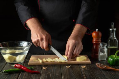 Mutfakta kızartma pişirmeden önce aşçı patatesleri küçük parçalara ayırır. Bıçaklı bir şefin elleri. Restoran veya otel için sebze diyeti menüsü