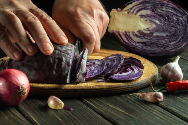 Aşçının elleri mutfak kesme tahtasındaki bıçakla kırmızı lahana kesti. Evde vejetaryen yemeği pişirmek.