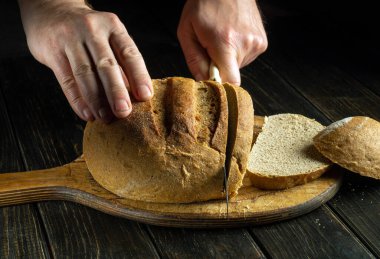 Bir aşçının elleri bıçakla restoran mutfağının kesme tahtasındaki fırınlanmış ekmeği keser. Sağlıklı beslenme ve geleneksel yemek kavramı.
