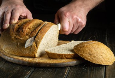 The chef hands with a knife slices bread on a kitchen cutting board. The concept of healthy food in the bakery. Copy space