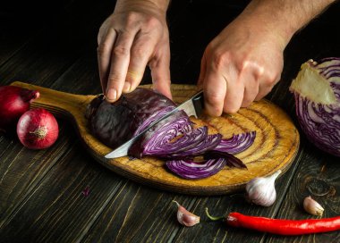The hands of the cook are cutting red cabbage on a cutting board with a knife. Cooking vegetable salad in the kitchen table. The idea of a vegetable diet. Copy space