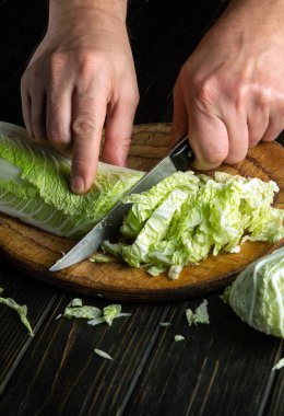The hands of the cook with a knife cut fresh lettuce leaves on a cutting kitchen board for vitamin salad. Diet menu for lunch or dinner