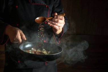 The cook adds pepper to a hot frying pan. The idea of European cuisine for a hotel with an advertising platform. Cooking fried vegetables in the kitchen