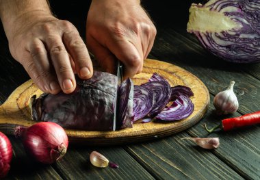 Hands of the chef with a knife cut red cabbage on a cutting board. Cooking vegetable salad in the restaurant kitchen. The idea of a vegetable diet