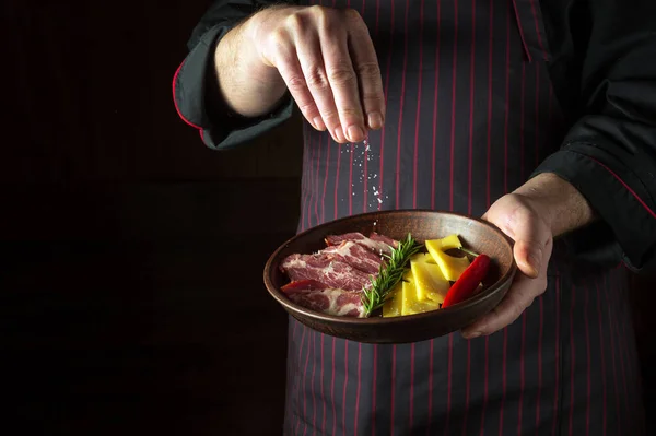 The cook sprinkles salt on a sliced steak with beef and cheese in a plate. The concept of serving dishes to order by the waiter or presentation