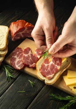 The chef makes open-faced ham and cheese tapas-style sandwiches on the kitchen table. Dark space for recipe or menu. Delicious fast food idea