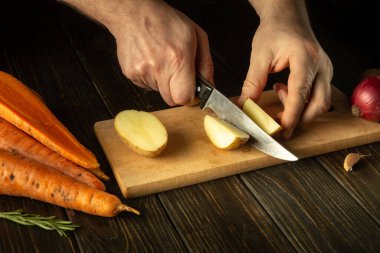 Aşçı bir bıçakla çiğ patatesleri küçük parçalara ayırır. Mutfakta çalışırken aşçıya yakın çekim. Lezzetli bir kahvaltı ya da akşam yemeği.