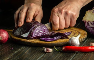 Aşçının elleri bıçakla kesilmiş kırmızı lahana ile salata için mutfak tahtasının üzerinde. Evde vejetaryen yemeği pişirmek.