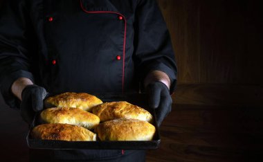 Profesyonel aşçı fırında pişmiş çörek ya da turta ile birlikte bir yemek tepsisi tutuyor. Menü ya da yemek tarifi için karanlık alan. Lezzetli turtaların sunumu