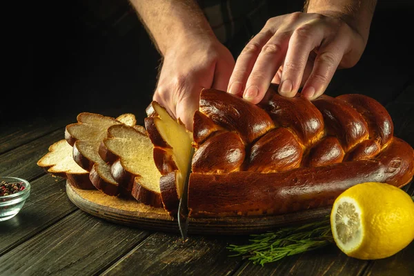 stock image Whole grain bread put on kitchen wood board with a chef holding knife for cut. Fresh bread on table close-up. Wheat kolach on the kitchen table or the healthy eating and traditional bakery concept.