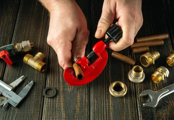 A plumber cuts a copper pipe with a pipe cutter. Installation or repair of gas equipment in the workshop on the table.