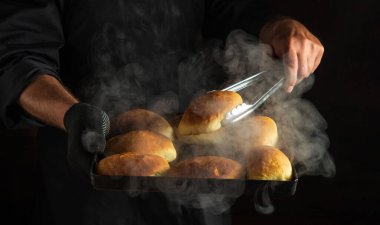 Sadece fırın eldiveni içinde sıcak bir fırın tepsisinde fırında pişmiş çörekler var. Aşçı, aşçı aletine bir çörek alır. Boşluğu kopyala