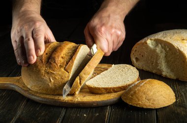 Aşçının elleri, fırın mutfağının ahşap tahtasında buğday ekmeğiyle tatmak için kesilmiş. Siyah arka planda sağlıklı gıda kavramı