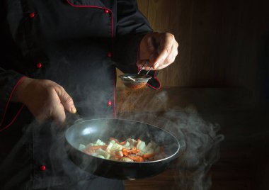 Profesyonel şef kızartma tavasında kızarmış havuç ve soğana kırmızı biber ekler. Öğle yemeği için sebze pişiriyorum. Karanlık bir arkaplanda restoran ya da otel menüsü