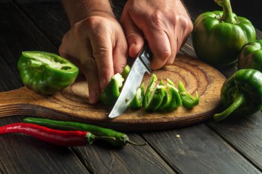 Ahşap kesme tahtasının üzerinde taze yeşil biberlerle kesilmiş bir aşçının elleri. Vejetaryen yemekleri hazırlarken şefin ellerini yakın plan çek. 