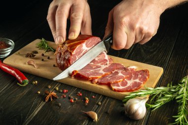 Aşçının elleri kesme tahtasının üzerinde ızgara et ile kesilmiş. Mutfak masasında baharat ve baharatlarla birlikte çalışma ortamı. Restoran menüsü için siyah arkaplan