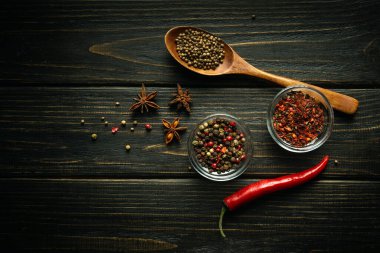 Siyah bir masada çeşitli baharatlar ve biberler. Cam bardaklarda ve kaşıkta baharatlar. Tarif veya menü için karanlık boşluk.
