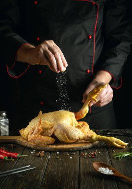 Aşçı bir restoran mutfağında çiğ horoz tuzlar. Öğle yemeği için güzel kokulu baharatlı ve biberiyeli horoz pişirmek. Güney usulü kızarmış tavuk