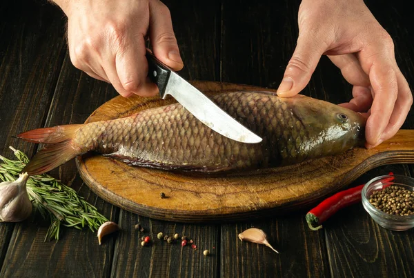 stock image The cook cuts fresh fish on a wooden cutting board with knife. Home cooking of a delicious fish dish according to an old recipe.