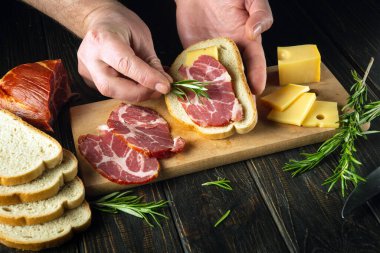 Açık yüzlü jambon ve peynirli tapas tarzı sandviçler mutfak tahtasındaki deneyimli bir aşçının elinden çıktı. Sandviçe aromatik biberiye ekliyorum.