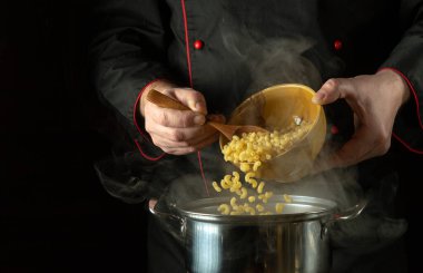 Aşçı makarnayı tavaya kaşıklıyor. Tarif ya da menü için karanlık alan. Restoranın mutfağında lezzetli makarna pişirme fikri.