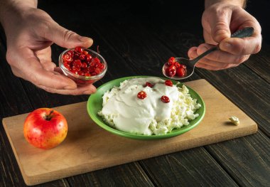 Aşçı ekşi kremalı süzme peynirli bir süt kahvaltısı hazırlar. Şef kaşıkla tatlı reçel ekliyor.