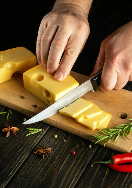 stock image Hands of the chef with a knife cut the cheese into small pieces for tasting. Delicious Milk Cheese Recipe Presentation. Black space for recipe