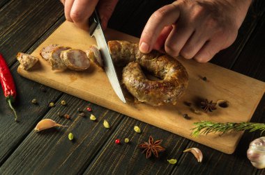 Mutfaktaki kesme tahtasındaki sosisleri aşçının elinden bıçakla kesmek. Ulusal yemek tatillerde baharatlarla hazırlanır..