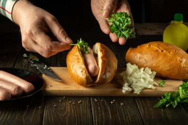 Şef sosisliye maydanoz koyar. Fast food konsepti mutfakta pişiyor.