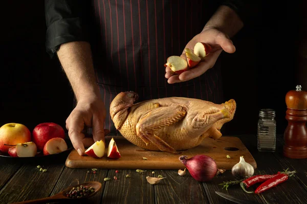 Adding apples to raw duck before cooking by the cook\'s hands. Raw duck on the kitchen table and cutting board. Working environment in a restaurant kitchen.